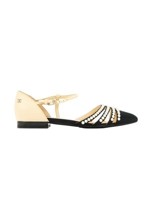 Chaussure plate pointue noire avec bride beige à la cheville et talon, décorée de perles blanches et d'un petit logo sur le talon.