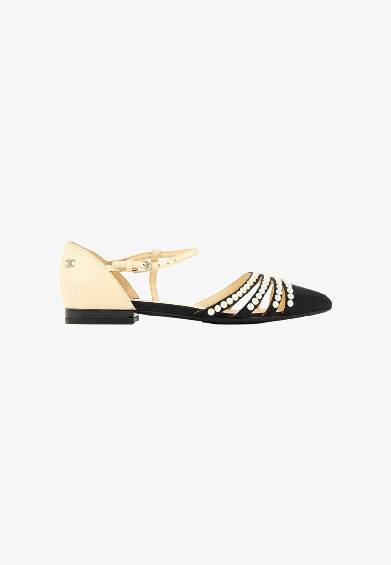 Chaussure plate pointue noire avec bride beige à la cheville et talon, décorée de perles blanches et d'un petit logo sur le talon.