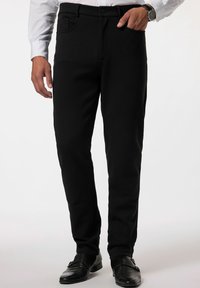 Pantaloni neri in cotone misto con vestibilità slim, dotati di tasca frontale, chiusura con bottone e dettagli di cucitura discreti. Indossati con scarpe nere.
