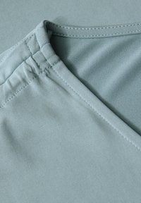 Tissu bleu clair avec une texture lisse, présentant un décolleté incurvé et des détails de couture aux coutures. Doux, extensible et adapté à un usage décontracté.