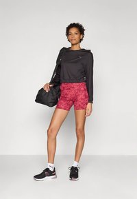 Sort cropped langærmet top, lyserøde mønstrede shorts, sorte sneakers og en sort skuldertaske. Velegnet til atletiske aktiviteter.