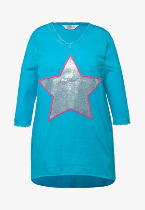 Turkusowa, oversize koszula z dekoltem w kształcie litery V, z dużym srebrnym wzorem gwiazdy obrysowanym na różowo. Rękawy mają długość 3/4 i postrzępione mankiety.