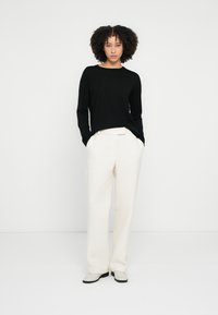 Black long-sleeve sweater paired with cream textured wide-leg trousers and light gray ankle boots, against a white background.