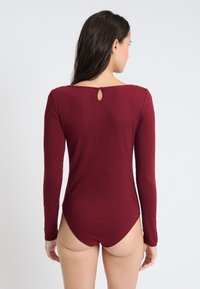 Bordeauxfarbenes Langarm-Bodysuit mit rundem Rückenausschnitt und einem Schlitzdetail, aus weichem, dehnbarem Material für Komfort und Bewegungsfreiheit.