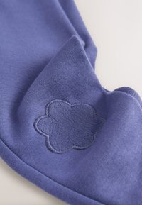 Țesătură mov cu o textură moale, prezentând un design brodat de floare pufoasă pe lateral. Țesătura are un finisaj neted, mat.