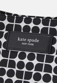 Czarnobiały materiał w geometryczny wzór z czarną prostokątną metką z napisem "kate spade NEW YORK" w białym kolorze.