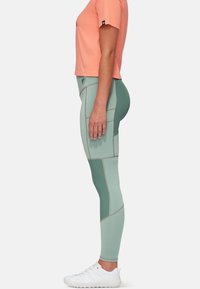 Leggings atletici verdi con pannelli a contrasto e cuciture, abbinati a una t-shirt attillata color corallo e scarpe da ginnastica bianche.