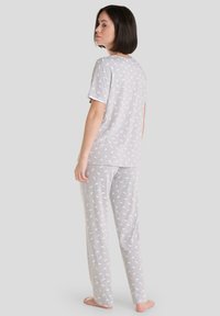 Conjunto de pijama gris en tela suave, que presenta una camiseta de manga corta con un patrón de hojas blancas y pantalones sueltos a juego con elementos de diseño similares.