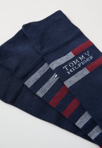 Chaussettes en coton bleu marine avec des motifs rayés rouges et blancs. Présentent le logo "TOMMY HILFIGER" brodé en blanc. Texture lisse.