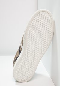 Semelle de sneaker en daim brun, caoutchouc blanc avec un motif hexagonal texturé. Accents latéraux en noir et blanc. Design épuré et moderne.