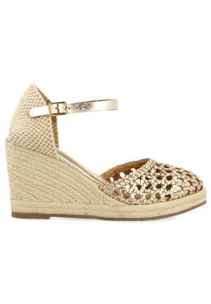 Chaussure espadrille à talon compensé avec une tige tressée en or métallique, une semelle intermédiaire en jute beige tressé et une bride de cheville ajustable.