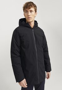 Sort isoleret jakke med hætte, der har en frontlynlås, sidelommer og en glat overflade. Designet med en let afslappet silhuet.
