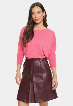 Rosa übergroßer Pullover mit Dreiviertelärmeln, kombiniert mit einem bordeauxfarbenen Lederfaltenrock mit hoher Taille und vorderer Nahtdetails.