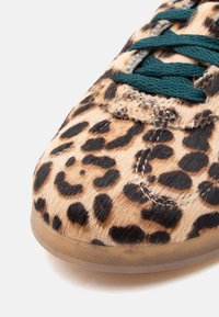 Αθλητικό παπούτσι με σχέδιο λεοπάρ, επιφάνεια με υφή που μοιάζει με γούνα, πράσινη κορδόνι, στρογγυλεμένη μύτη και λαστιχένια σόλα με διαφανές άκρο.
