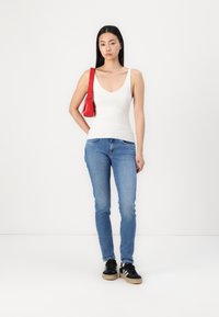 Canotta bianca a costine, jeans skinny blu, sneakers nere con suola chiara e una piccola borsa rossa con tracolla.