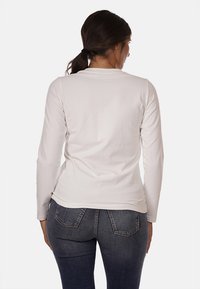 Maglia a maniche lunghe di un leggero beige, realizzata in morbido cotone, con scollo rotondo, design aderente e texture liscia, indossata con jeans scuri.