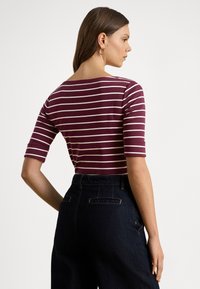 Top ajustado às riscas em bordô e branco com mangas curtas, com decote barco, combinado com calças de ganga escuras de cintura alta.