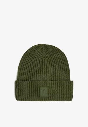 Zelená žebrovaná pletená čepice s ohrnutým lemem a čtvercovou nášivkou na přední straně. Měkká textura a elastický materiál.