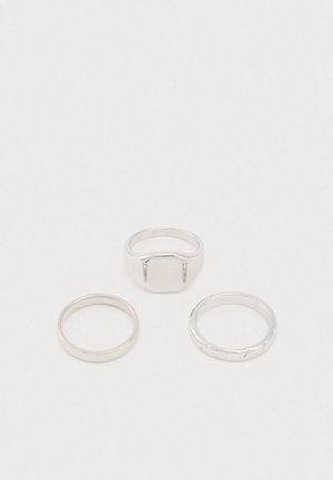 Set van drie zilveren ringen: één gepolijste band, één met een vierkante bovenkant en één met een gedraaide textuur.