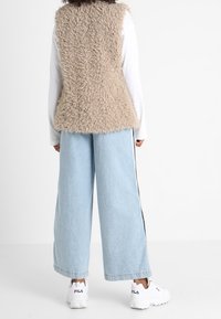 Beige, texturerad faux fur-väst med ärmlös design, kombinerad med ljusblå vida jeans och vita sneakers. Enkel, avslappnad outfit.