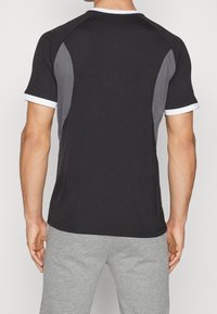 Camiseta deportiva negra con inserciones de malla gris en los laterales, acentos en el cuello en blanco y un diseño ajustado, combinada con pantalones de chándal grises.