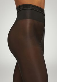Sorte gennemsigtige strømpebukser med en glat, blank overflade og en bred talje med m�ærkenavnet "Wolford" i diskret print.