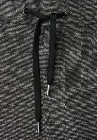 Jogging gris texturé avec une taille élastique à cordon, dotés de cordons noirs avec des embouts en métal argenté.