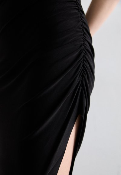 Abito nero con texture arricciata, caratterizzato da uno spacco alto fino alla coscia. Realizzato in tessuto liscio, mostra una silhouette aderenza e dettagli arricciati.