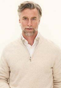 Beige ritssluiting trui gemaakt van zachte stof, met een hoge kraag en subtiele textuur, gelaagd over een witte overhemd met kraag.
