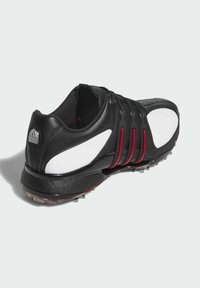 Czarno-białe buty sportowe z syntetyczną cholewką, czerwonymi akcentami, teksturowaną podeszwą oraz wieloma kolcami dla lepszej przyczepności. Zawierają logo na pięcie.