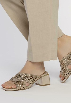 Sandalias slip-on de oro con tacón cuadrado. Presentan un diseño de tiras entrecruzadas y punta abierta. Textura suave, adecuadas para el uso casual.