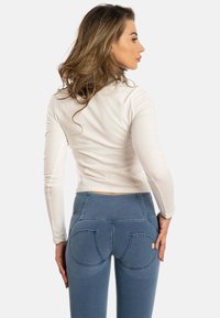 Un haut beige clair à manches longues associé à un jean bleu ajusté avec des poches arrière courbées uniques et de subtils détails de couture.