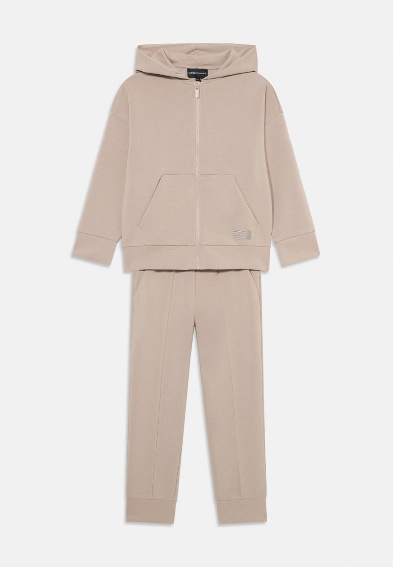 Beige Kapuzen-Sweatshirt mit Reißverschluss und vorderer Tasche, kombiniert mit passenden schmal geschnittenen Hosen, beide aus weichem Stoff mit gerippten Bündchen.