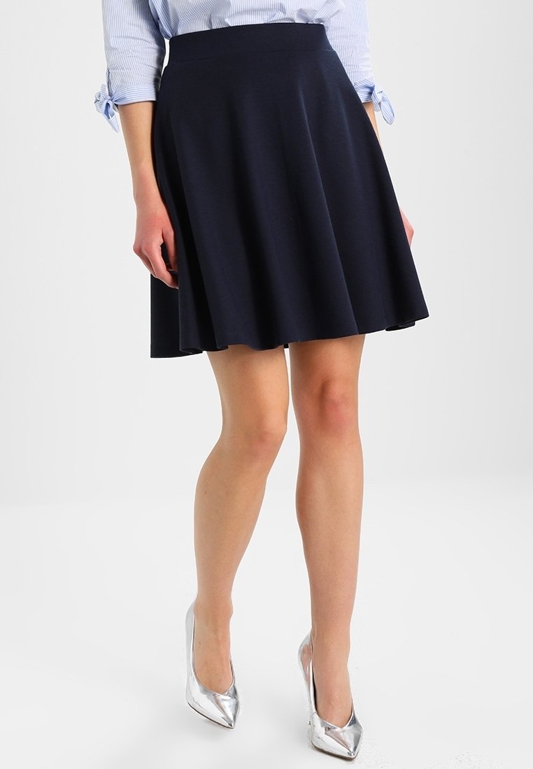 Marineblauer ausgestellter Rock aus Stoff mit glatter Textur und enger Taille. Kombiniert mit silbernen High Heels für einen Kontrast.