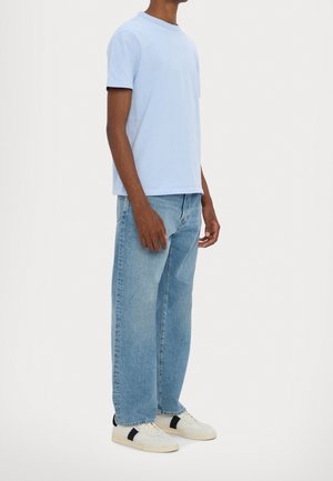 T-shirt en coton bleu clair à manches courtes, assorti à un jean en denim bleu clair à coupe ample et des baskets blanches avec des accents noirs.