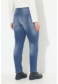 Vihreät siniharmaat farkut suoralinjaisella leikkauksella, joissa on kaksi takataskua ja keskikorkea vyötärö, yhdistetty mustiin kenkiin.