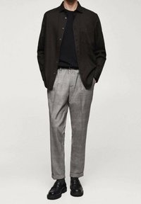 Chemise boutonnée marron foncé, associée à un pantalon à carreaux gris clair. Des chaussures noires complètent la tenue, avec un design et une texture élégants.