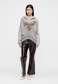 Felpa grigia con grafica di aquila e coulisse, abbinata a pantaloni lucidi di colore bordeaux scuro. La felpa ha polsini e orlo a coste.