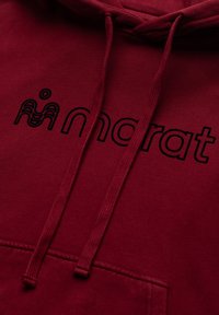 Bordowa bluza z kapturem ze ściągaczami i czarnym obrysem napisu "mandrat" na piersi, z stylizowanym logo fali nad literą "m".