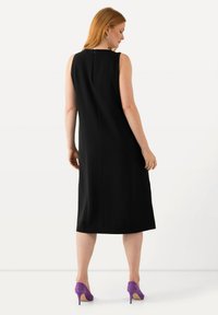 Vestido negro sin mangas con una silueta recta, cremallera trasera y dobladillo hasta la rodilla. Combinado con zapatos de tacón altos morados.