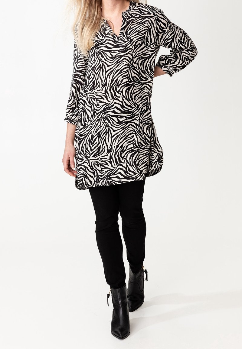 Black and white zebra print tunic top with three-quarter sleeves, paired with black skinny pants and ankle boots. Smooth fabric texture.