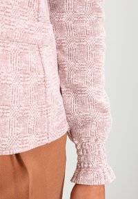 Ljusrosa mönstrad tröja med texturerad tyg, med samlade ärmhål och avslappnad passform. Matchad med ljusbruna byxor.