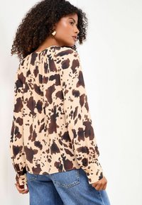 Blusa beige a maniche lunghe con stampa leopardata marrone scuro, caratterizzata da una vestibilità rilassata e polsini con bottoni, abbinata a denim blu.