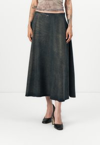 Denim maxi skjørt i mørk blå, med en klassisk A-linje silhuett, sidelommer og en jevn tekstur. Akkompagnert av svarte høye hæler.