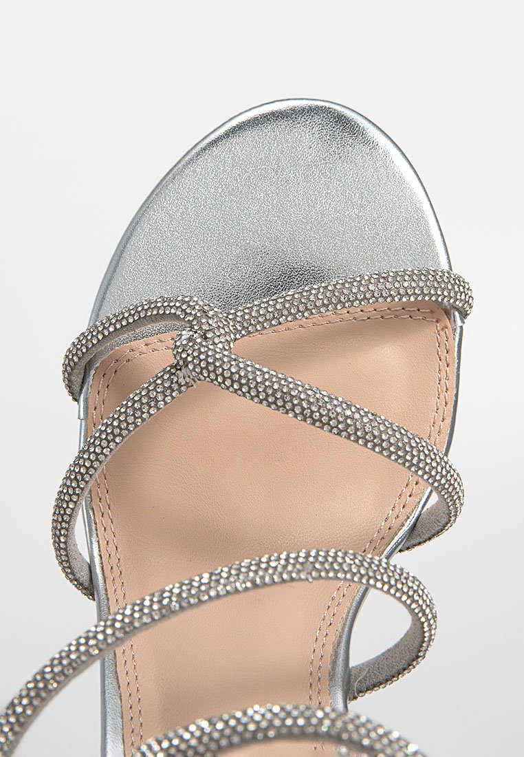 Zilveren hoge hak sandaal met kruislingse banden versierd met kleine rhinestones, met een gladde, metallic bovenkant en een beige binnenzool.