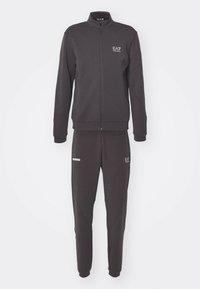 Tuta di colore grigio scuro realizzata in tessuto morbido, composta da una giacca con zip e colletto alto e pantaloni elasticizzati coordinati, entrambi con dettagli del logo.