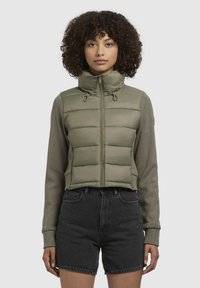 Jachetă verde măsliniu cu mâneci scurte, captusită, cu guler înalt, fermoar frontal și detalii cu șnur, asortată cu pantaloni scurți din denim negri.