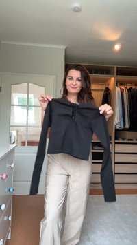 Musthave musta lühike-sleeve särk ümar kaelusega ja pitsist esiküljega detail, valmistatud venivast kangast, hoiab inimene seda kapitaustiku taustal.