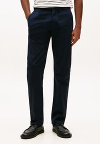 Pantalon chino bleu marine en coton, doté d'une coupe slim, de poches latérales et d'une texture lisse. Associé à des chaussures noires.
