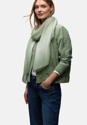 Giubbotto bomber verde chiaro con polsini e orlo a costine, abbinato a una sciarpa verde menta testurizzata. Indossato sopra una maglietta bianca e jeans blu.